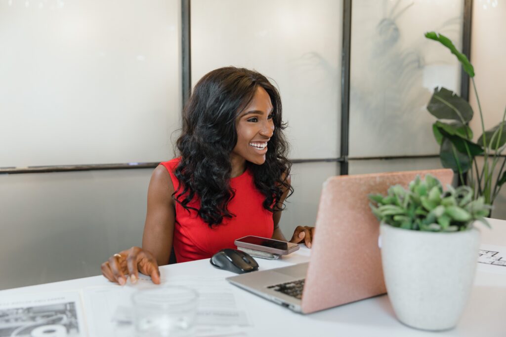 female entrepreneur smiling at pink laptop modern office