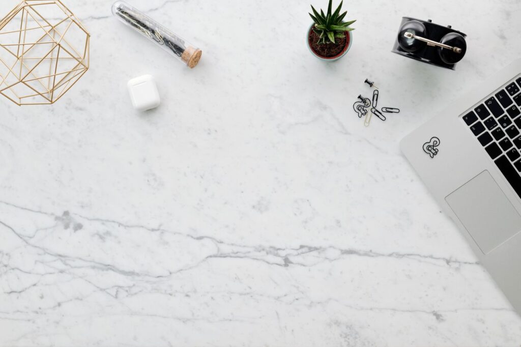 Stylish flat lay of a minimalist workspace featuring a laptop, plant, and geometric decor on a marble desk.
