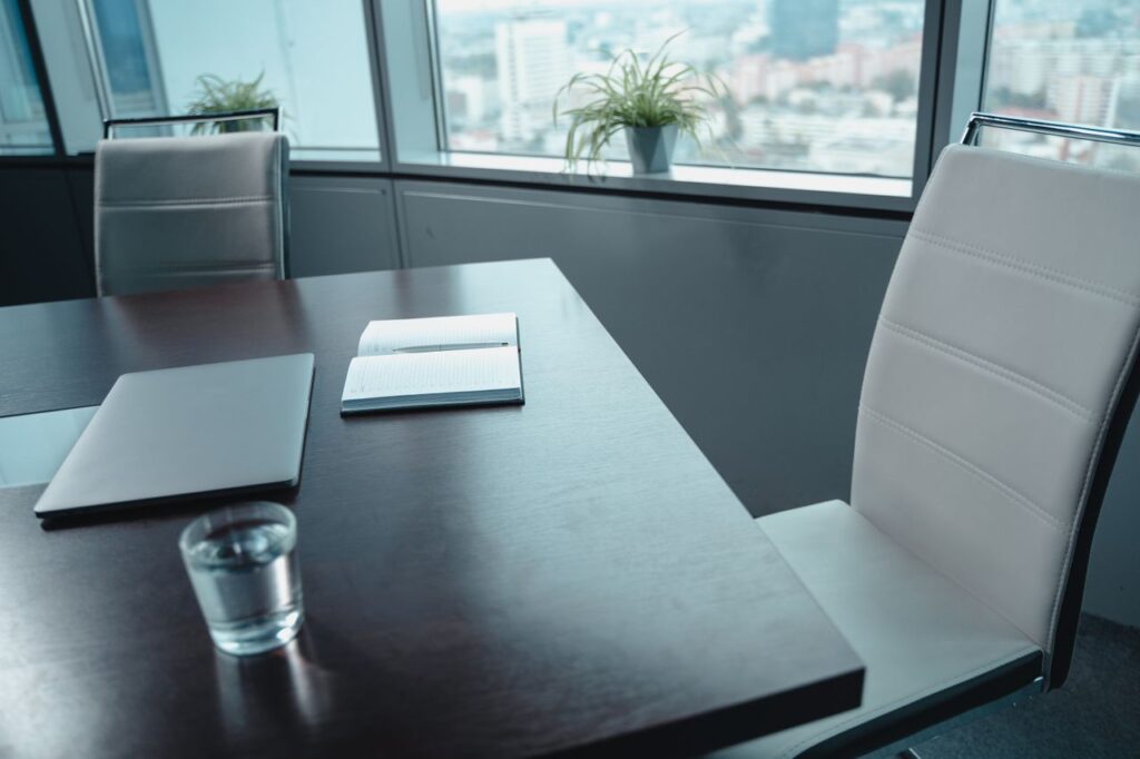 Sleek office conference room setup with laptop, notebook, and glass of water on a table.